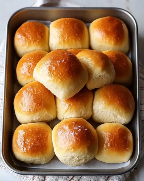 A tray of golden-brown dinner rolls arranged neatly, with one roll on top of others.