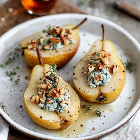 A plate of baked pear halves stuffed with blue cheese and topped with chopped walnuts and fresh thyme.