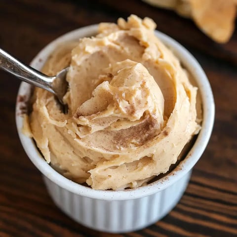 A close-up of creamy cinnamon butter in a white dish with a spoon resting inside.