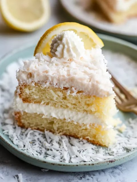 A slice of cake with white frosting and a lemon wedge on top.