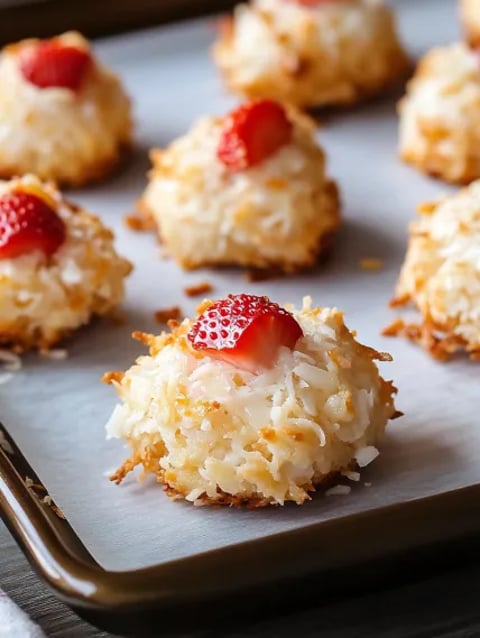 A tray of coconut cookies with strawberries on top.