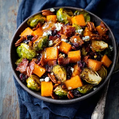 A bowl of food with bacon, brussels sprouts, and carrots.