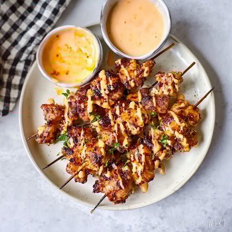 A plate of bang bang chicken skewers with sauce.