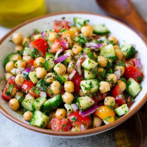 A bowl of chickpea salad with tomatoes, onions, and cucumbers.