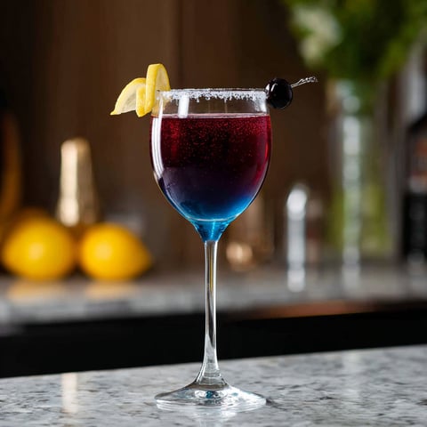 A glass of Midnight Kiss Cocktail with a lemon wedge on top.