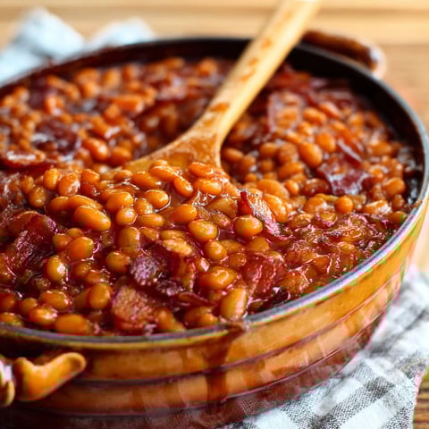 A bowl of baked beans with a wooden spoon in it.