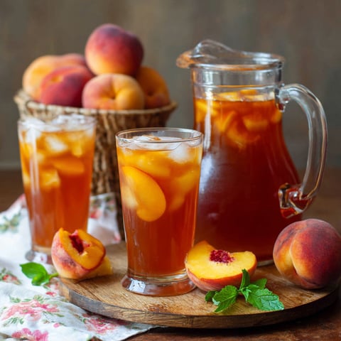 A glass of sweet peach iced tea with a peach slice in it.